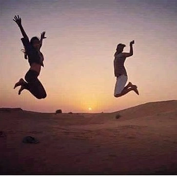 Travelers jumping for joy on the sand dunes at sunset